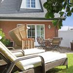 Garten mit Liegestühlen, Tisch und Stühlen vor einem Haus mit rotem Backstein und weißem Zaun.