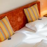 Double bed with white sheets and striped pillows against a wooden headboard.