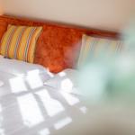 A bed with white sheets and an orange headboard. Two pillows with striped pattern.