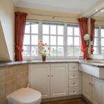 Bathroom with window, sink, and toilet. White cabinets and red curtains.