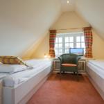 Two beds in an attic room with window and chair.