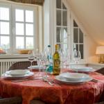 Dining table with tablecloth, glasses, and a wine bottle. Window and cabinet in the background.