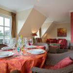 Dining table with tablecloth and glasses, living area with sofa and wall art.