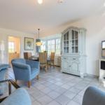 Living and dining area with blue seating, white furniture, and TV. Tile floor and large window.