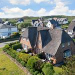 House with thatched roof and garden. Surroundings with other houses and hills.