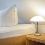 A bed with white pillows and a lamp on a wooden nightstand.