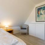 Bedroom with bed, nightstand, chair, and wardrobe under sloped ceiling.