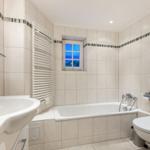 Bathroom with bathtub, toilet, and sink. Window shows view.