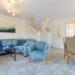 Living and dining area with blue sofa, staircase, and dining table with chairs.