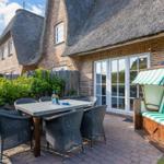 Terrace with table, chairs, and beach chair in front of a thatched-roof house.