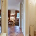 Hallway with hooks and view into living room with seating and windows.