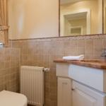 Bathroom with sink, mirror, and toilet. Walls covered with stone tiles.