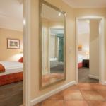 Bedroom with bed and window, bathroom with shower and bathtub, hallway with mirror and terracotta floor.