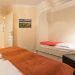Room with two beds, wall picture, and door in background.