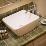 Sink with faucet on green tiled countertop with soap and toiletries.