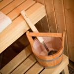 Sauna with wooden bench, white towel, and bucket with ladle.