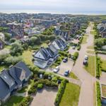 Aerial view of a coastal village with houses, gardens, and the sea in the background.