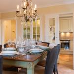 Dining room with set table and chandelier. Kitchen visible in background.