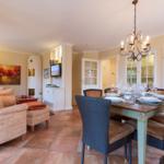 Dining area with table and chairs, living area with sofa and TV, terrace and kitchen visible.