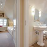 Bedroom with sloped ceiling and bathroom with pedestal sink.