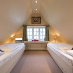 Two beds under sloped ceiling with window and curtains.