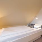 Bedroom with bed, table lamp, and wardrobe under sloped ceiling.