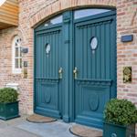 Two green front doors with round windows on a brick facade.