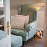 A green armchair with cushions and ottoman next to a lamp.