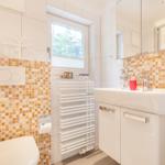 Badezimmer mit Waschbecken, Spiegel, Toilette und Fenster