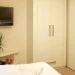 Schlafzimmer mit Bett, Kleiderschrank und Wandfernseher.