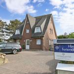 Haus mit Steinmauer, Parkplatz und Schild. Haus mit Dach und Fenstern.