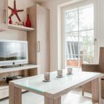 Wohnzimmer mit Fernseher, Glas-Tisch und Rattan-Stuhl vor großem Fenster.