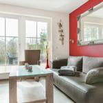 Wohnzimmer mit grauem Sofa, Glas-Tisch und roter Wand mit Spiegel.