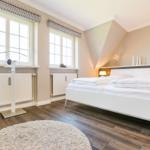 Bedroom with white bed, two windows, and wooden floor.