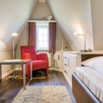 Bedroom with bed, red armchair, and desk under sloped ceilings.