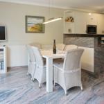 Dining area with table, chairs, and kitchen. Marble floor and wall picture.