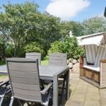 Terrace with table, chairs, and wicker lounger. Background: greenery and trees.