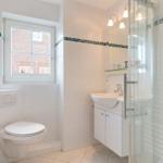 Badezimmer mit Dusche, Waschbecken und Toilette. Fenster mit Blick auf Gebäude.