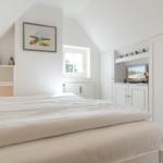 Schlafzimmer mit Bett, Schrank und Fenster. Wandbild und Vogelskulpturen.