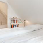 Schlafzimmer mit Dachschräge, Bett und Bücherregal. Bad ist angebaut.