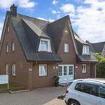 Ein zweistöckiges Haus mit rotem Ziegelstein und dunklem Dach. Vor dem Haus steht ein Auto.