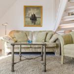 Wohnzimmer mit Sofa, Sessel und Glas-Tisch unter einer Treppe.