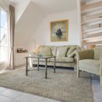 Wohnzimmer mit Sofa, Sessel und Terrassentür. Wandbild und Treppe sichtbar.