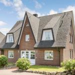 Two-story brick house with dormers and white entrance. Garden with flowers and stone wall.