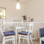 Dining area with white table, two chairs, and blue seat cushions. Background with sofa and railing.