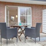 Outdoor area with table and two chairs in front of a house with brick wall and white doors.