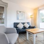 Wohnzimmer mit Sofa, Sessel und Tisch. Fenster mit Blick auf Grün.