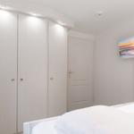 Schlafzimmer mit weißem Bett, Kleiderschrank und Wandbild.