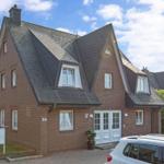 Haus mit rotem Ziegelbau und dunklem Schieferdach. Weiße Fenster und Tür. Parkplatz vorne.