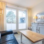 Wohnzimmer mit Sofa, Tisch und TV. Fenster mit Vorhängen und Blick nach draußen.